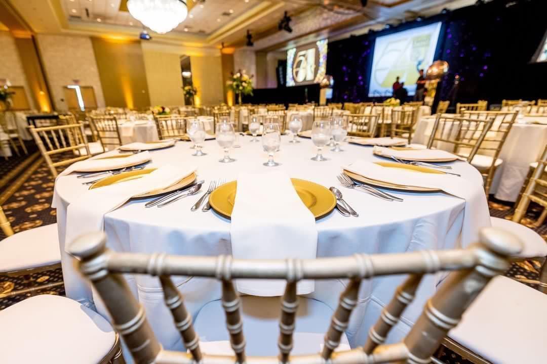 Round banquet tables set for a formal event in an elegant ballroom with gold chairs and stage lighting