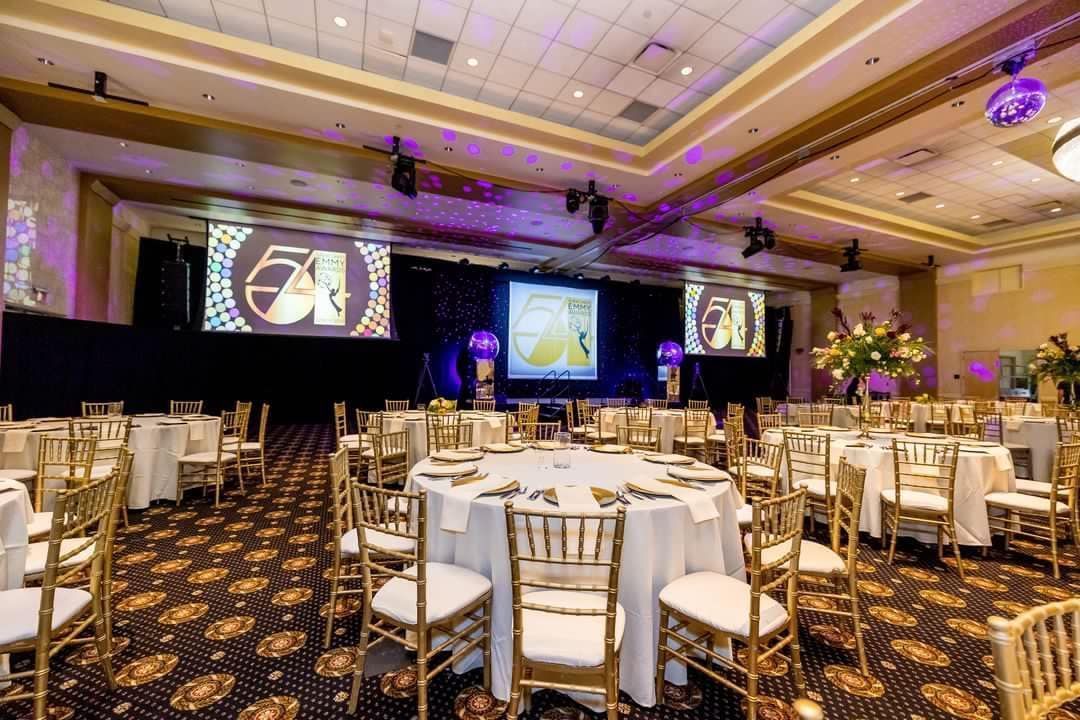 Elegant banquet hall with round tables, gold chairs, and purple stage lighting for an event