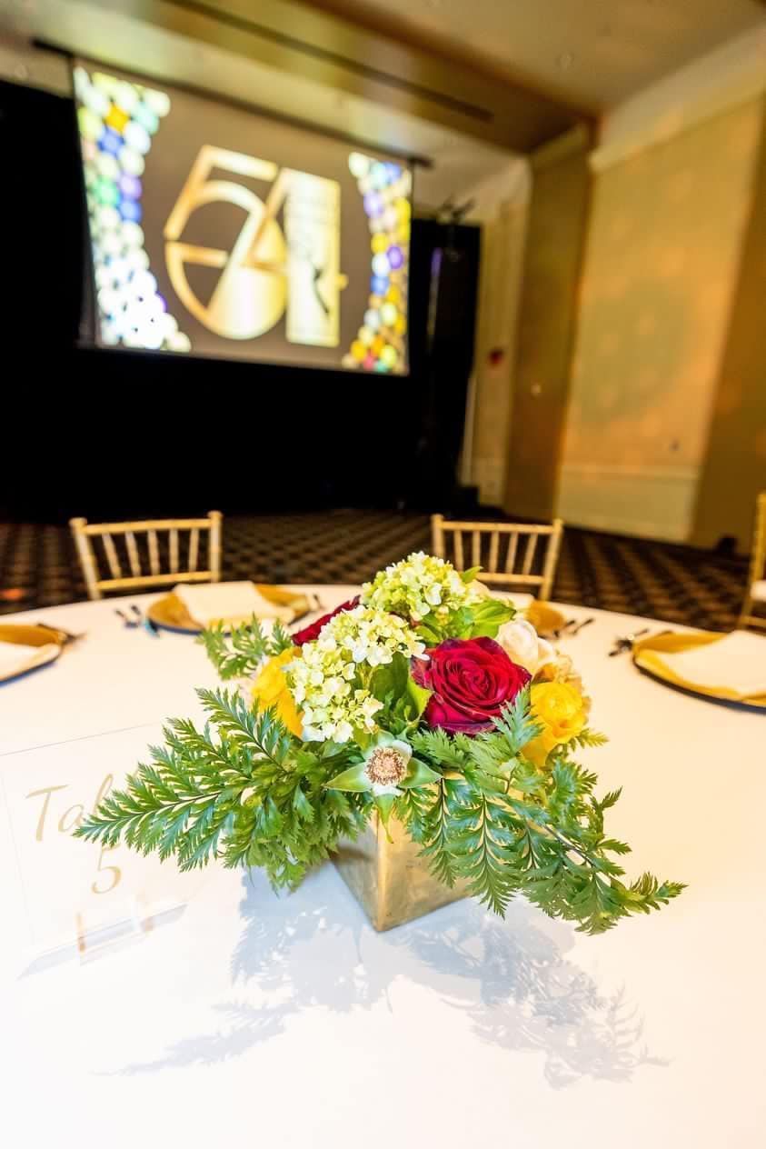 Floral centerpiece on a banquet table before a projected 60th anniversary screen