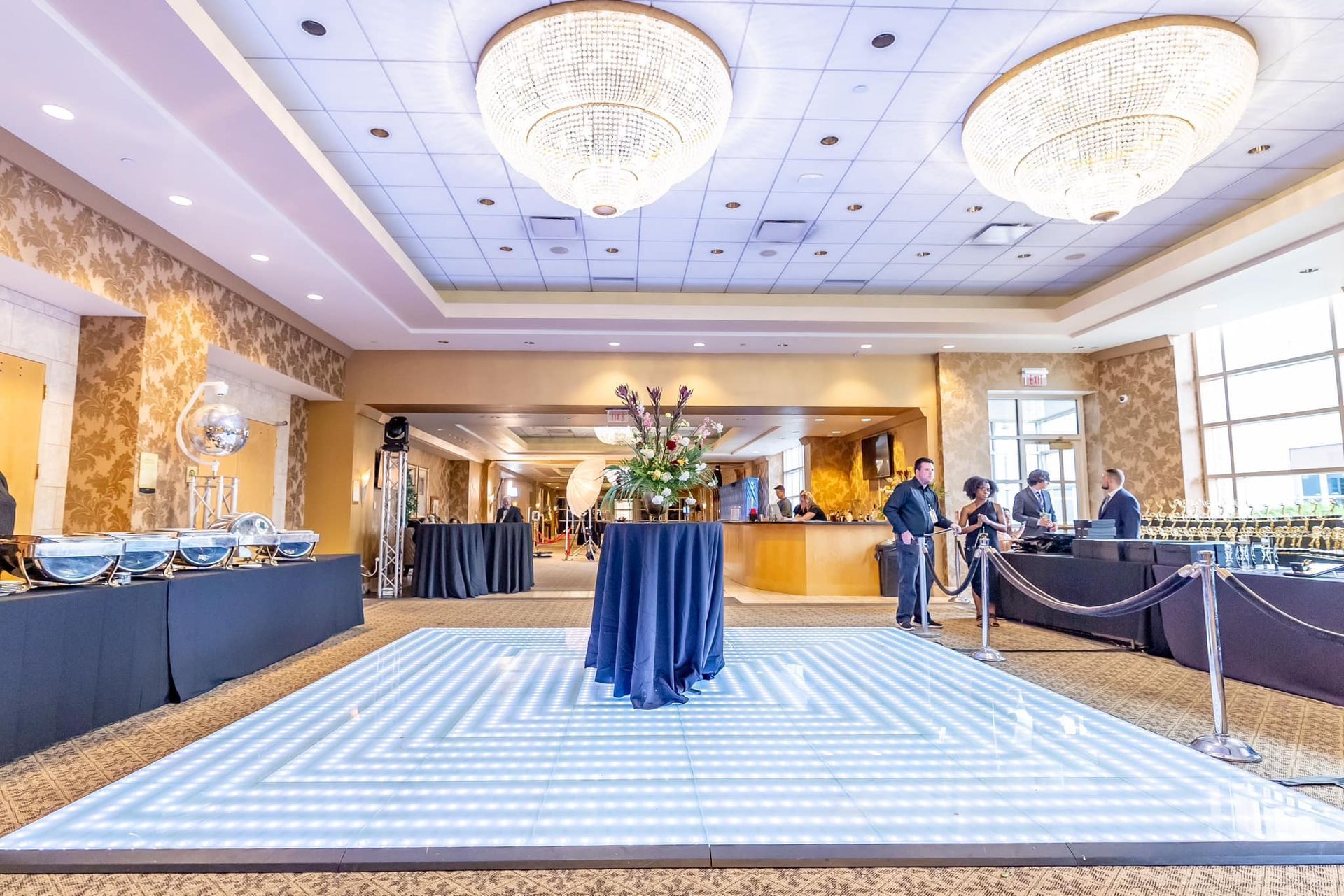 Bright hotel lobby with chandeliers, check-in counter, and a blue cocktail table in the center