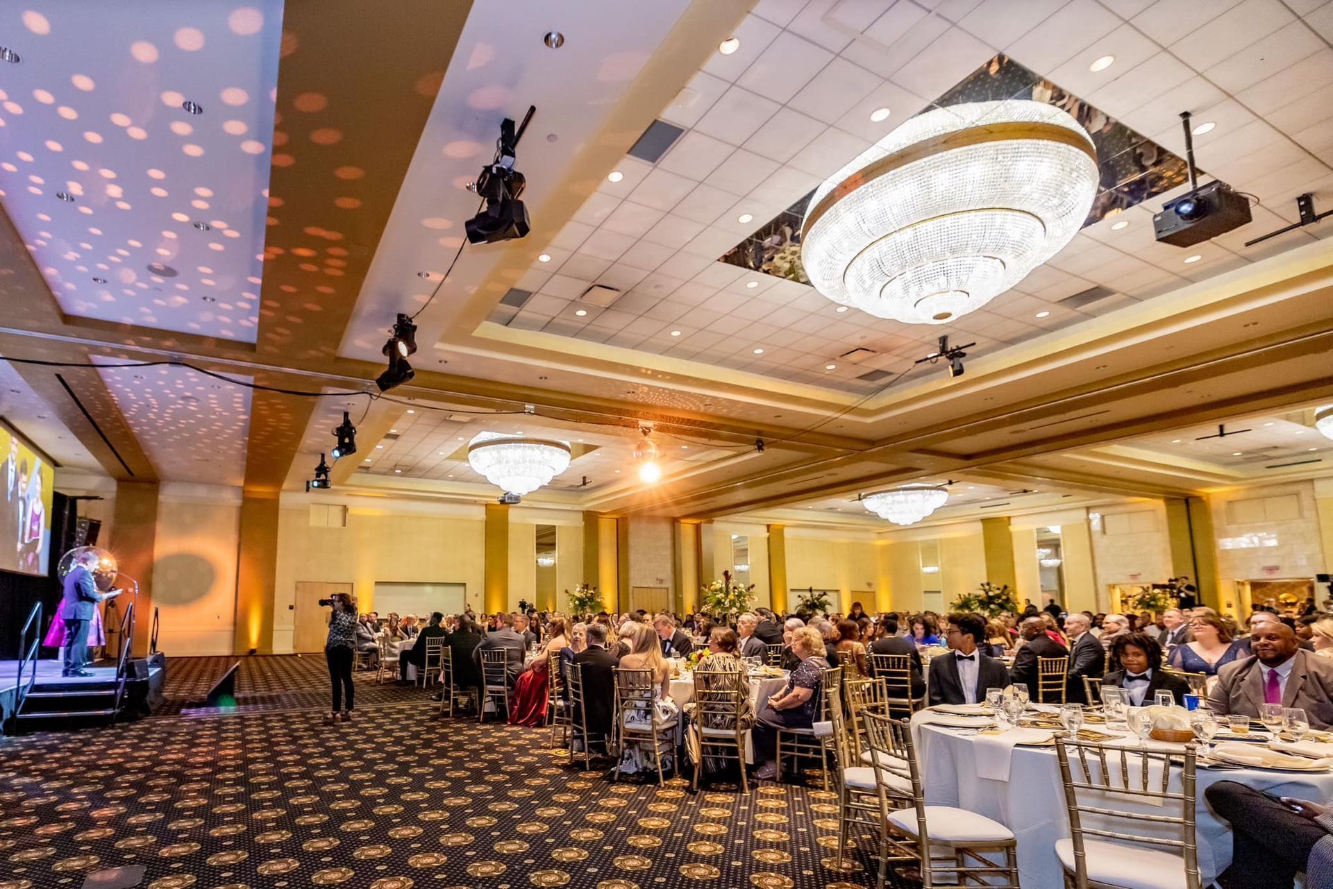 Banquet hall with guests seated at round tables under chandeliers during a formal event