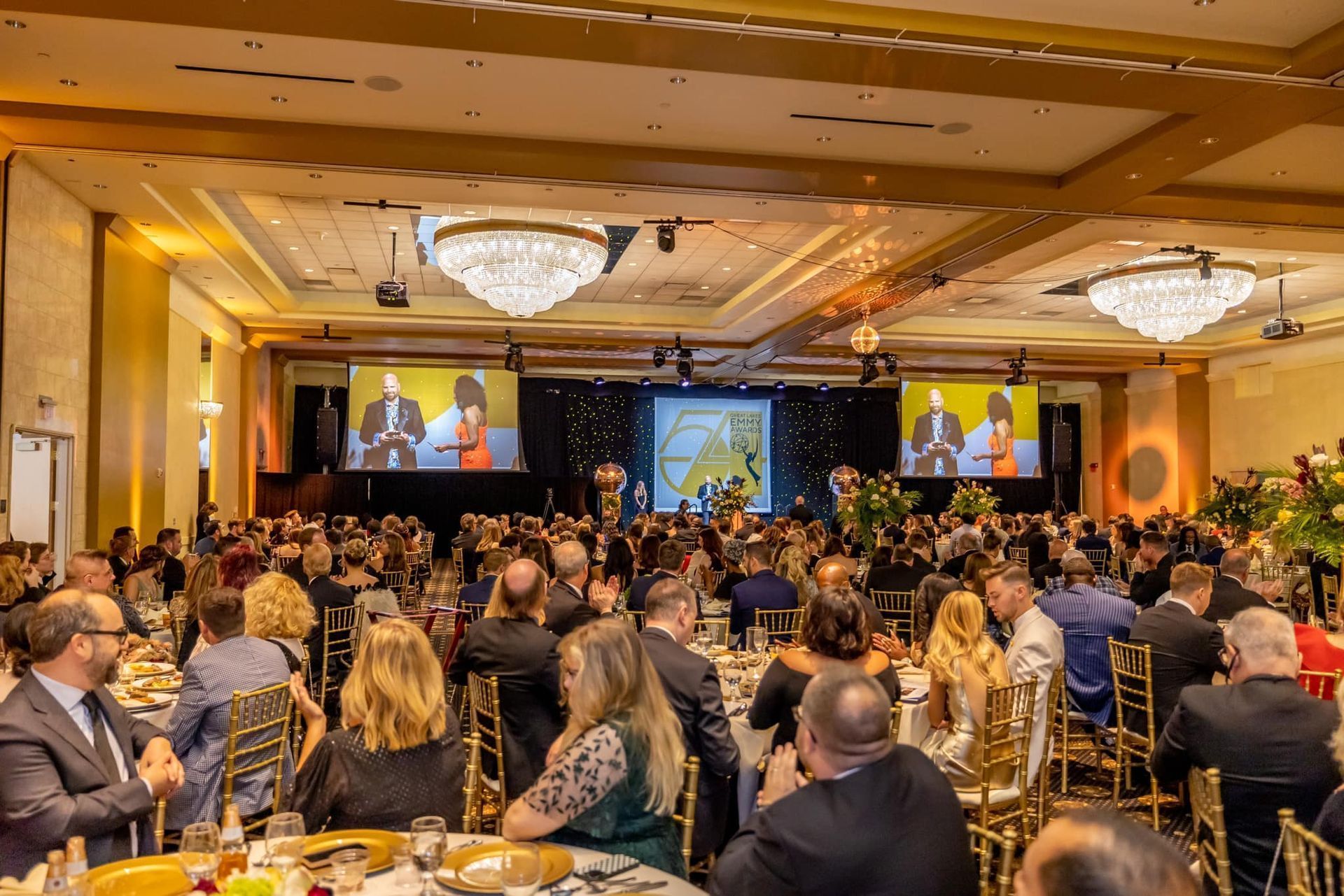 Conference ballroom with a large audience facing two screens and a stage at the front