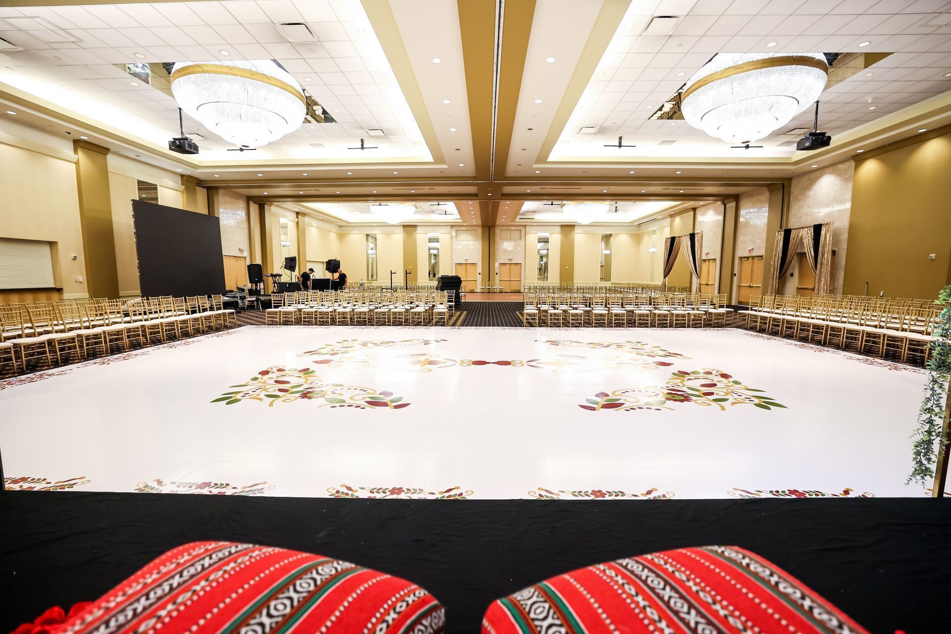 Large banquet hall with a long U-shaped table, white floral floor design, and gold chandeliers