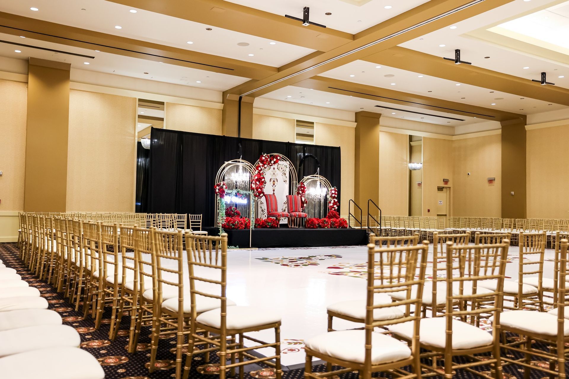 Elegant banquet hall with rows of gold chairs facing a decorated stage and black curtain backdrop