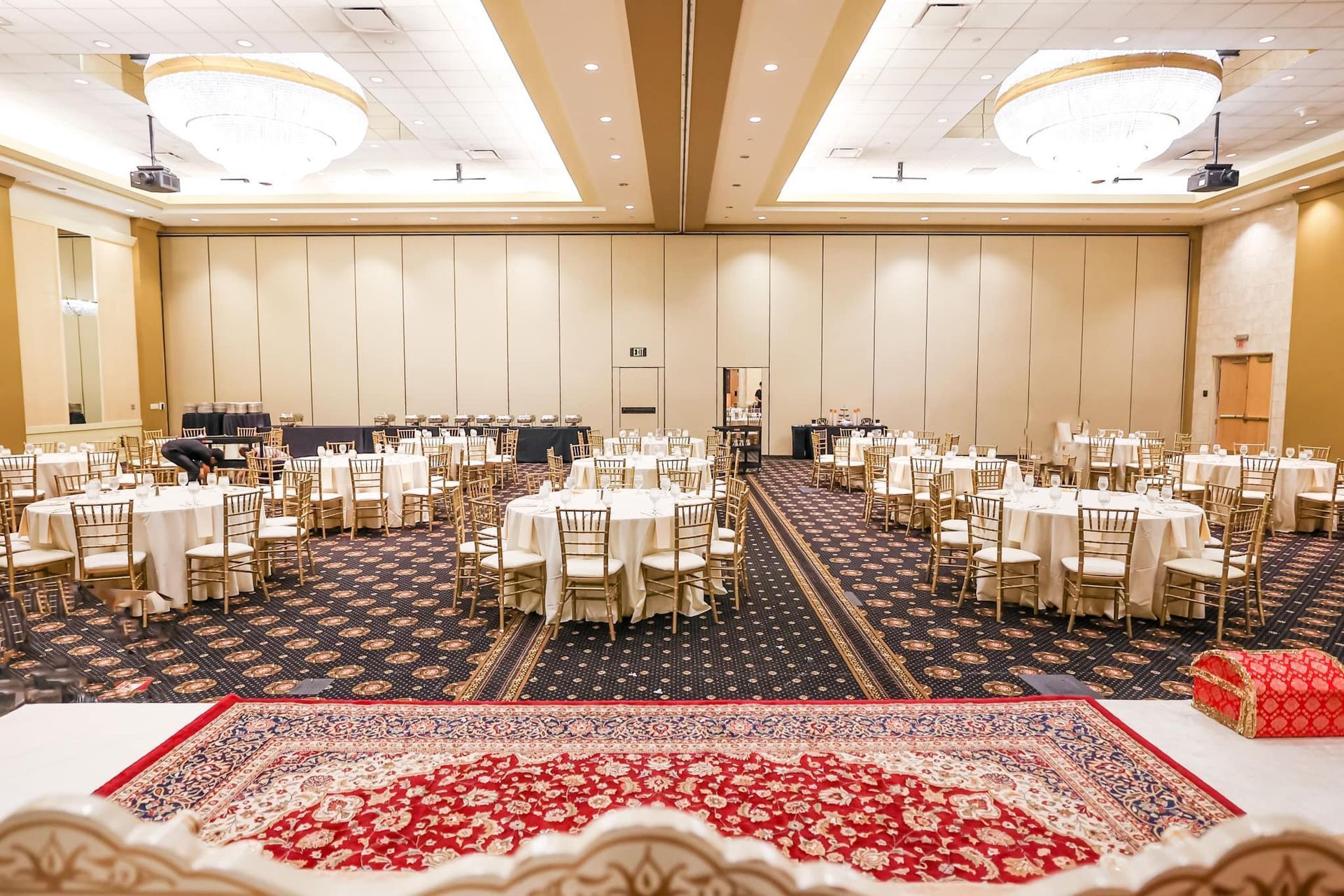 Elegant banquet hall with round tables, white chairs, and patterned carpet under warm ceiling lights