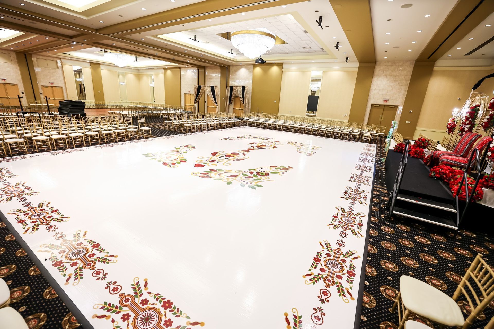 Large banquet hall with rows of chairs, a white dance floor, and floral decor around the edges.