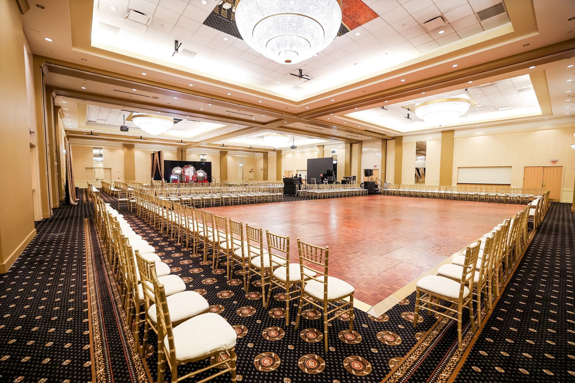 Empty ballroom with rows of gold chairs around a glossy dance floor and chandeliers overhead