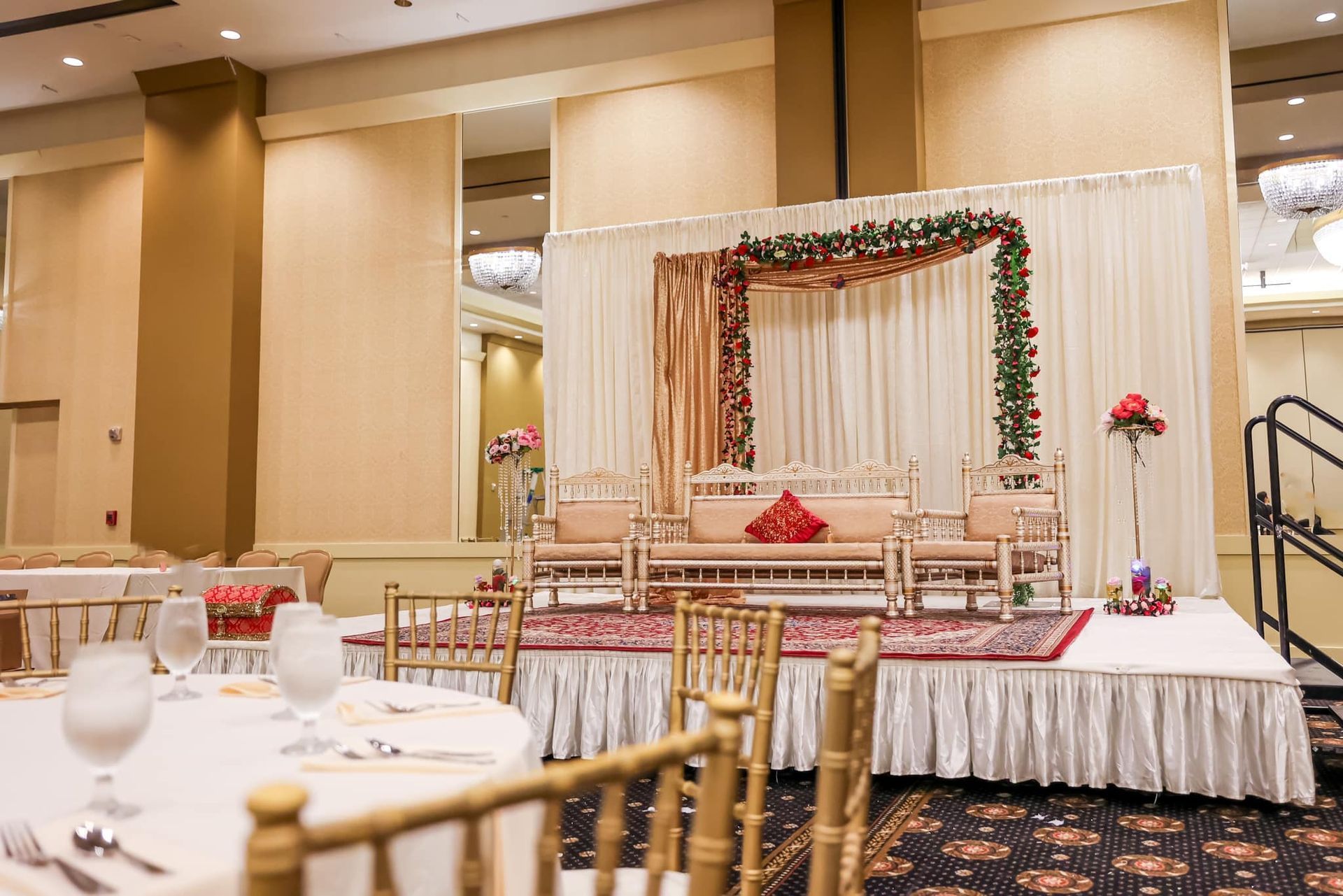 Decorated wedding stage with floral arch, draped curtains, and banquet tables in a reception hall