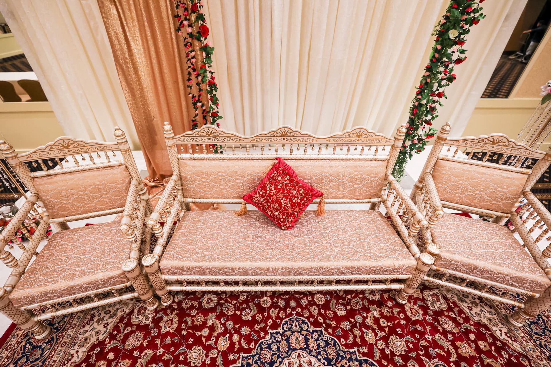 Elegant wedding stage with ornate cream sofas, red cushions, and floral drapes on a patterned carpet