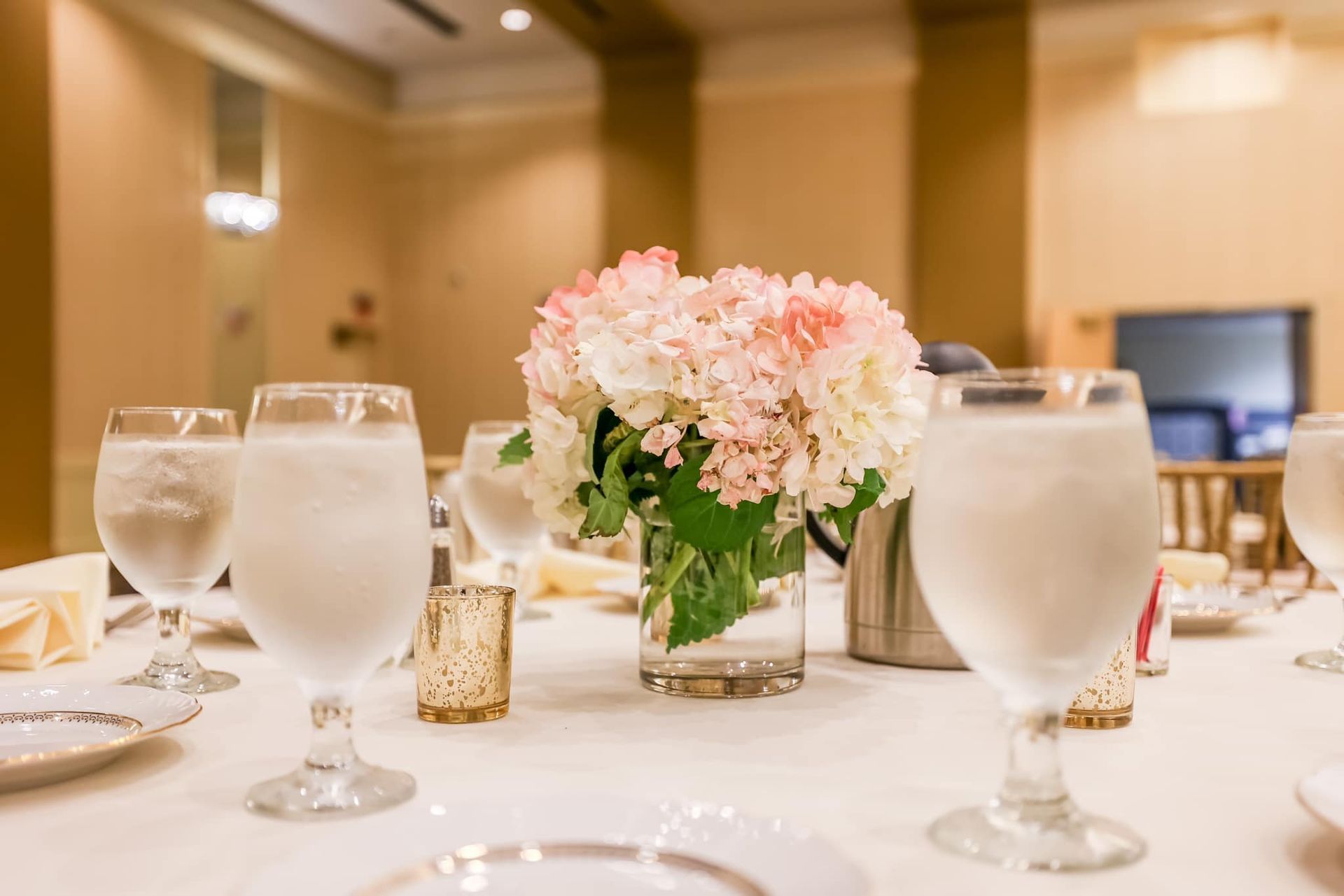 Elegant banquet table with water goblets and pink floral centerpiece in a warmly lit dining room
