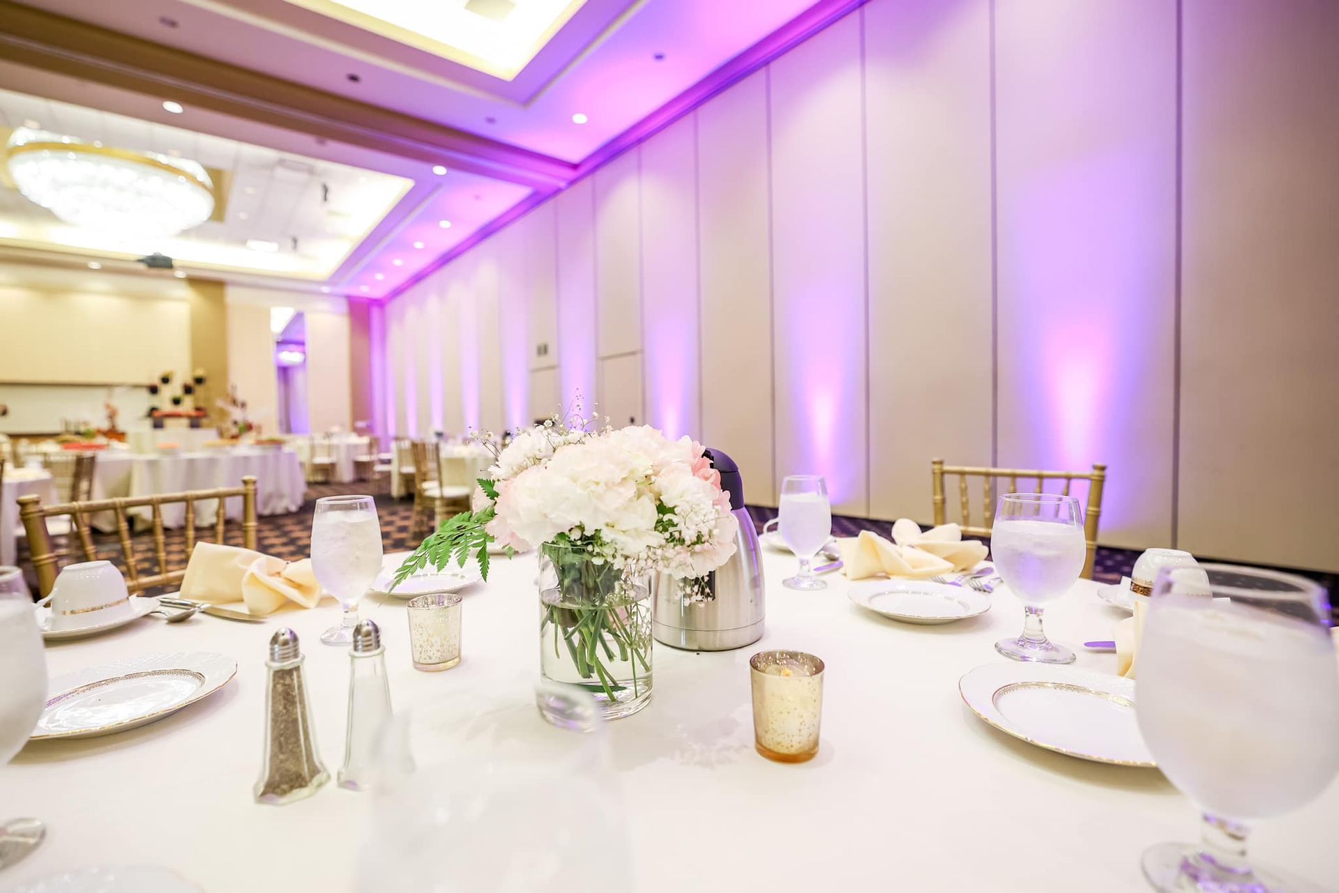 Elegant banquet hall with white table settings, floral centerpieces, and purple ambient lighting