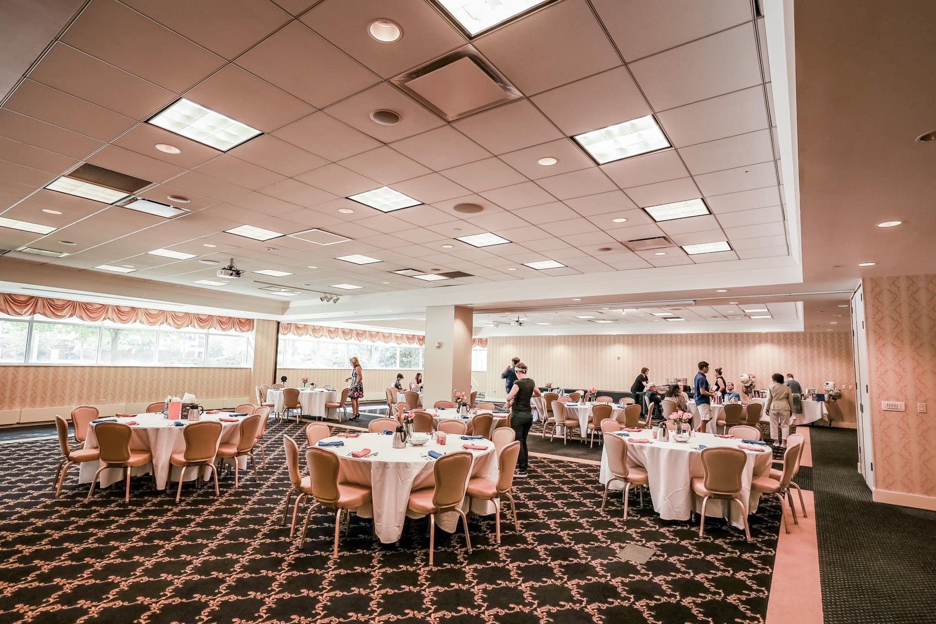 Banquet hall with round tables set for an event and a few people mingling in the background