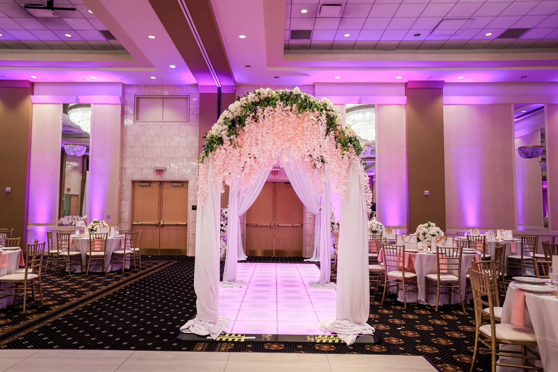 Wedding aisle with white floral arch in a purple-lit reception hall