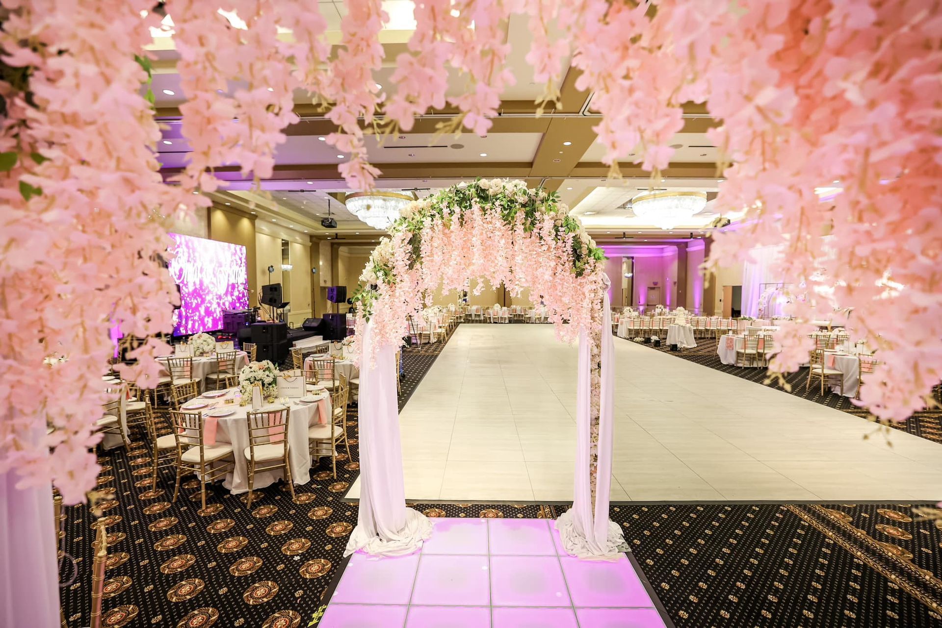 Pink floral archway in a decorated banquet hall aisle with tables and banquet seating