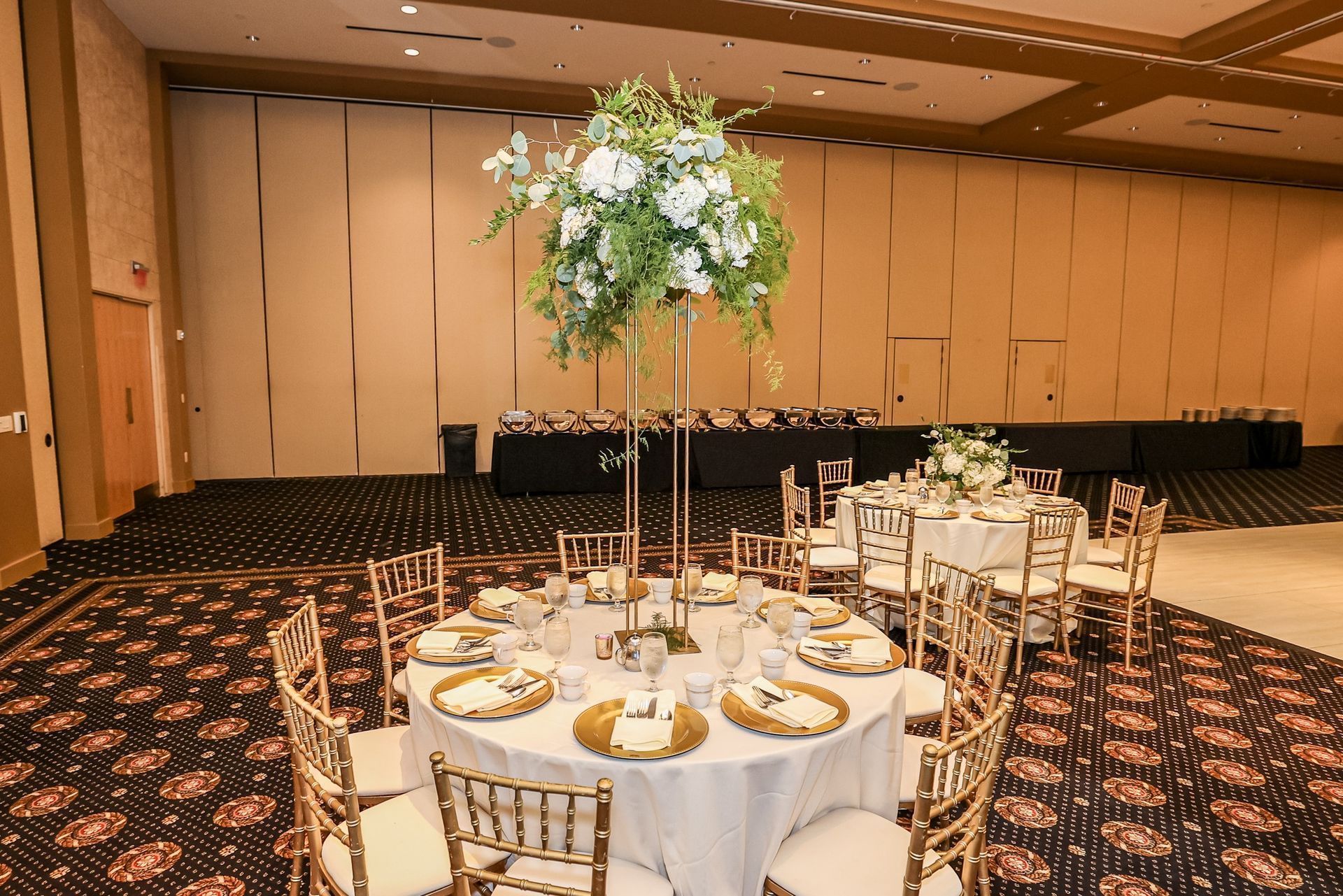Banquet hall with round tables set for a formal event and a tall white floral centerpiece