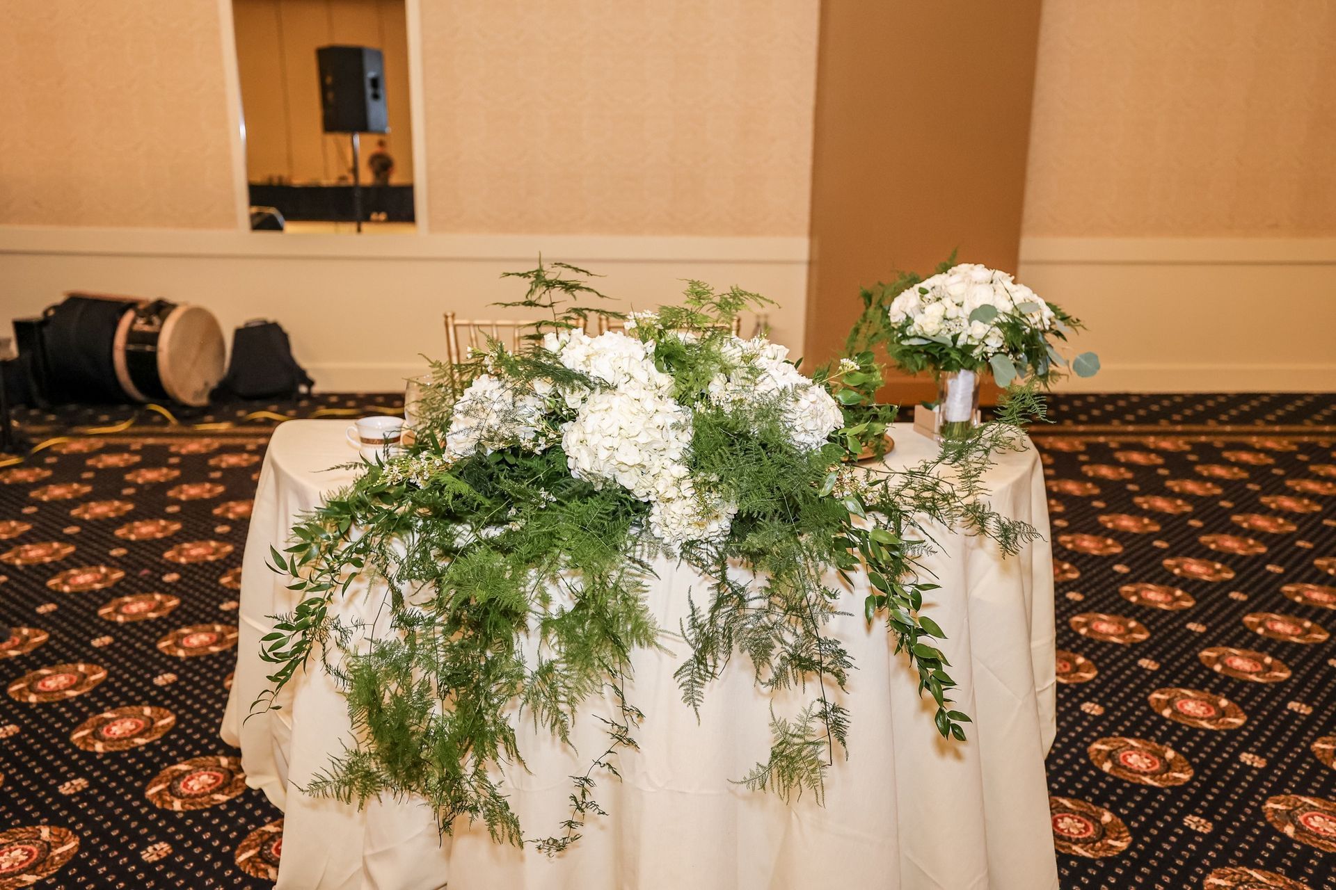 Floral arrangement of white flowers and greenery on a draped table in a banquet hall