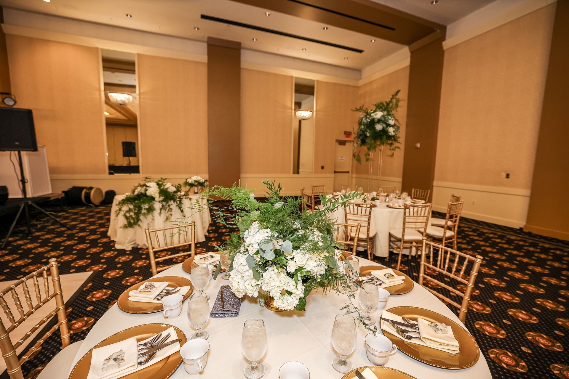 Elegant banquet hall with round tables set for a formal event, white floral centerpieces, and patterned carpet