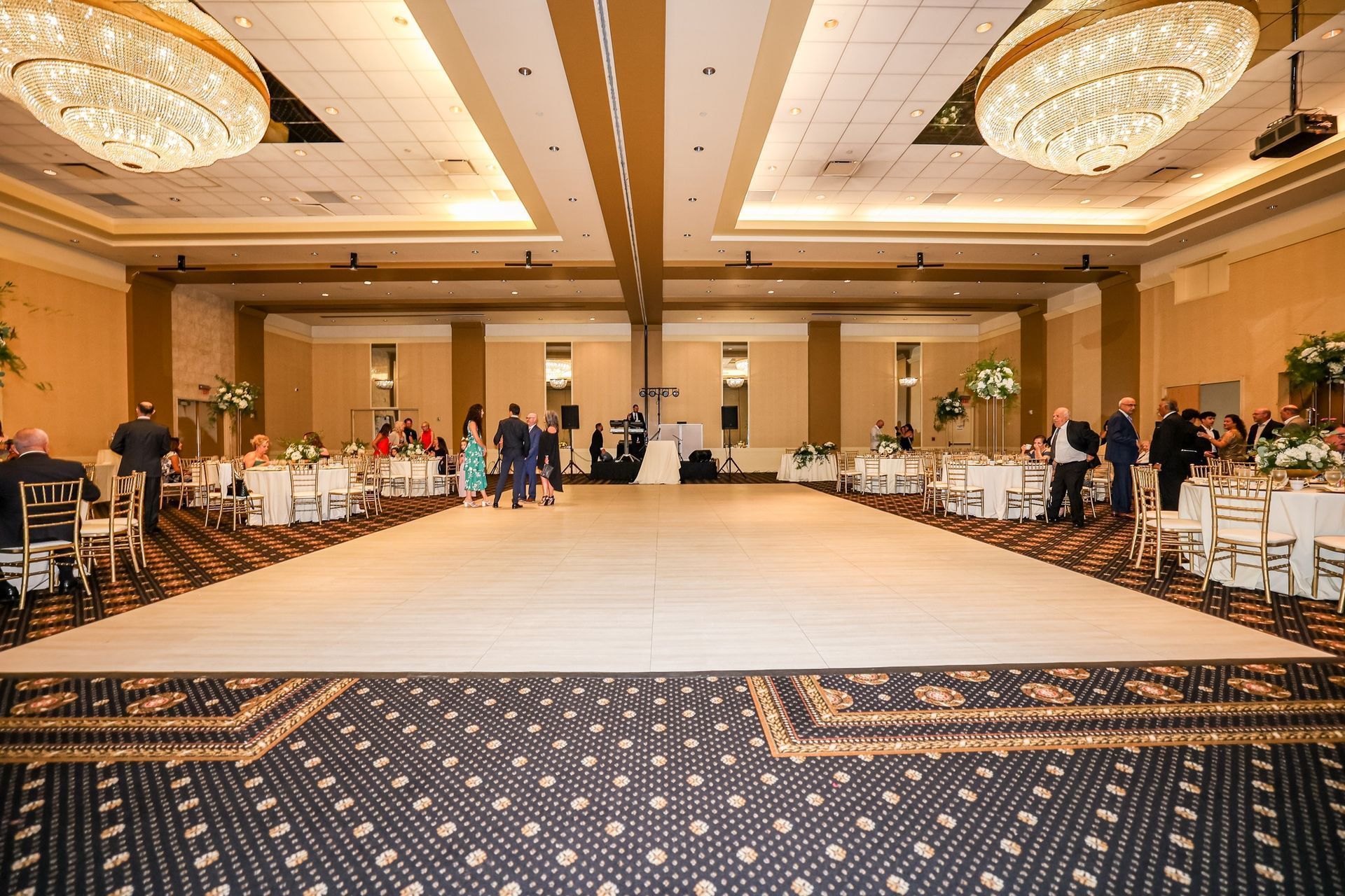 Grand ballroom with a wide dance floor, chandeliers, and guests seated along both sides.
