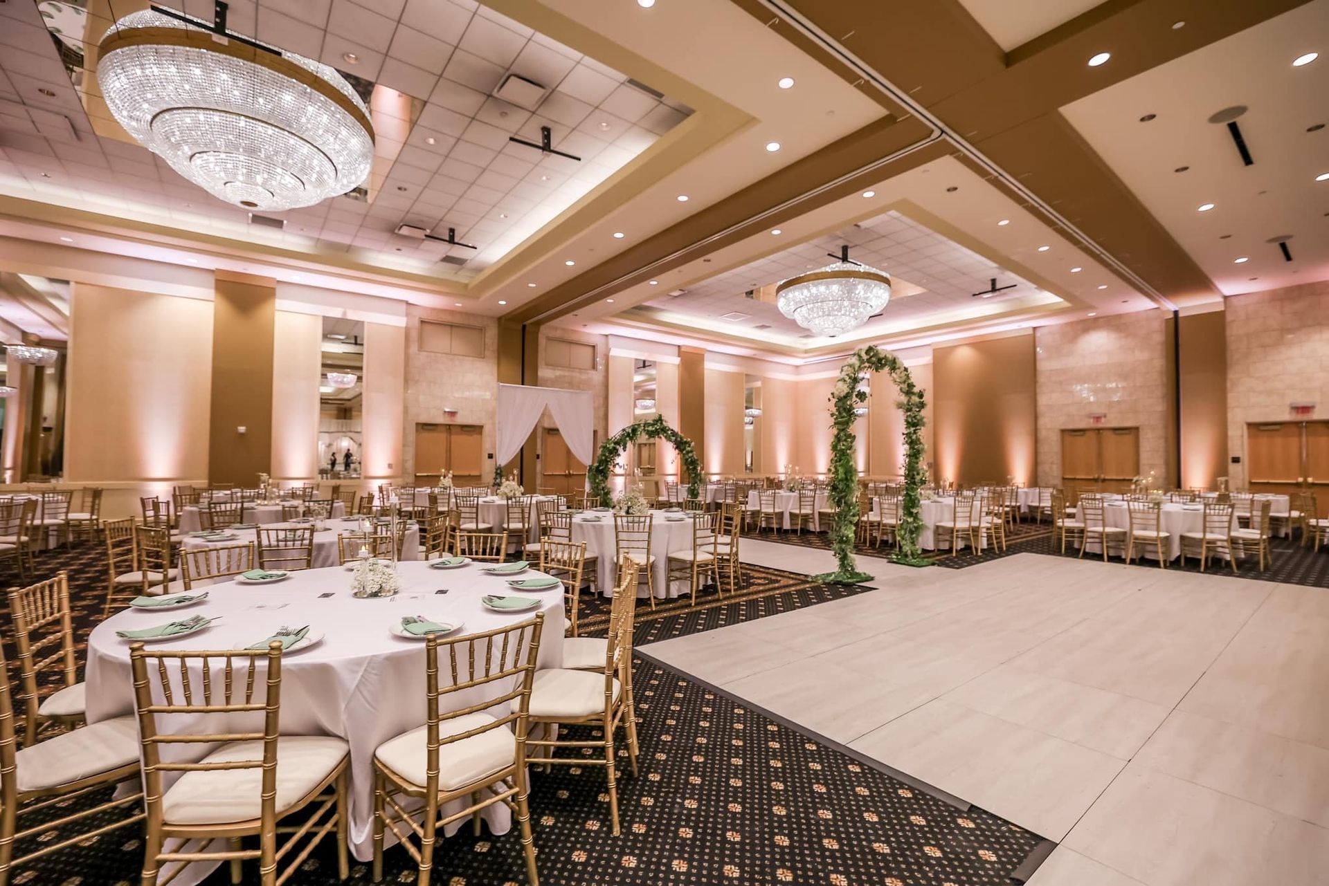 Elegant banquet hall with round tables, gold chairs, and chandeliers under warm lighting