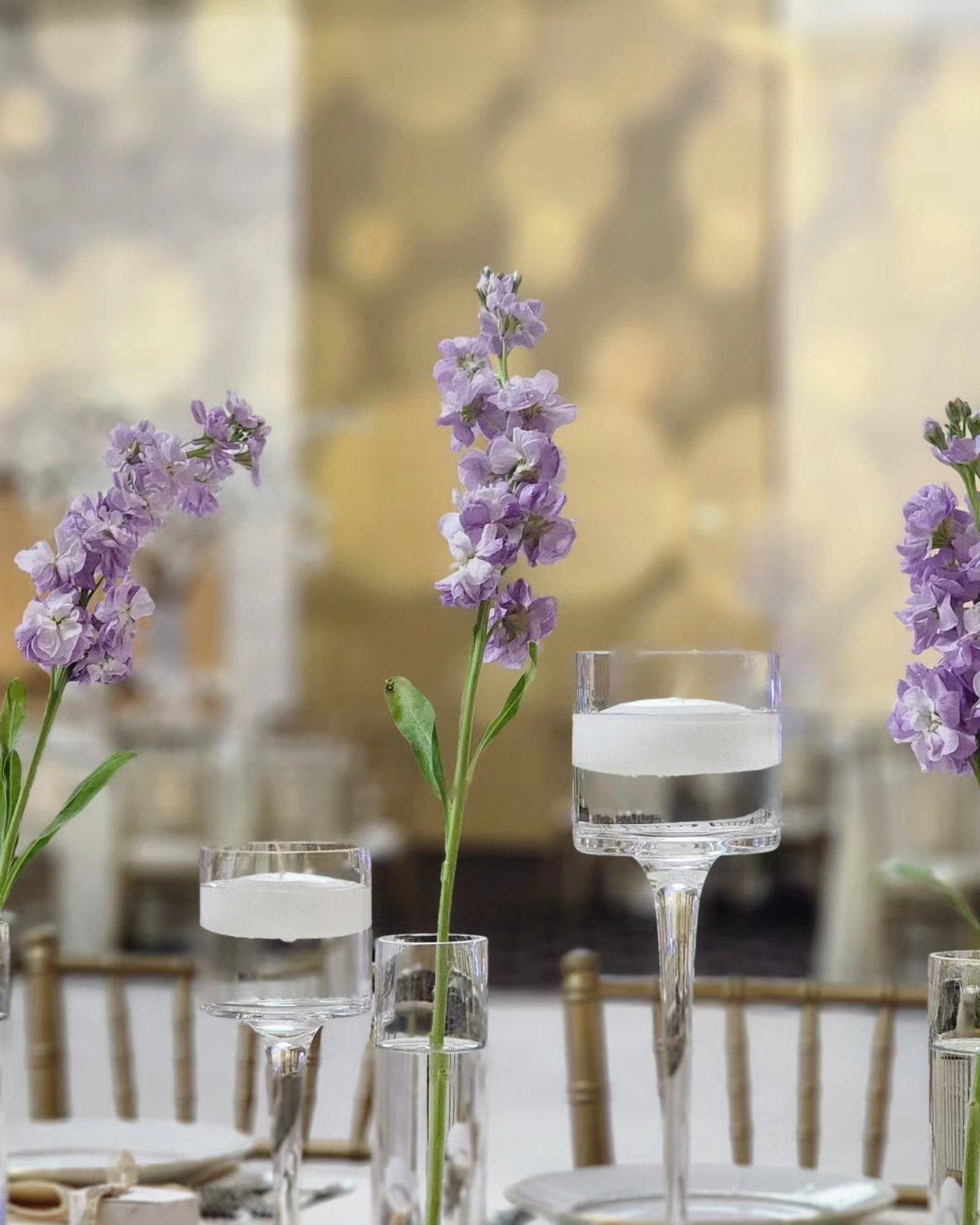Purple flowers in glass vases on a decorated table with candles and stemware