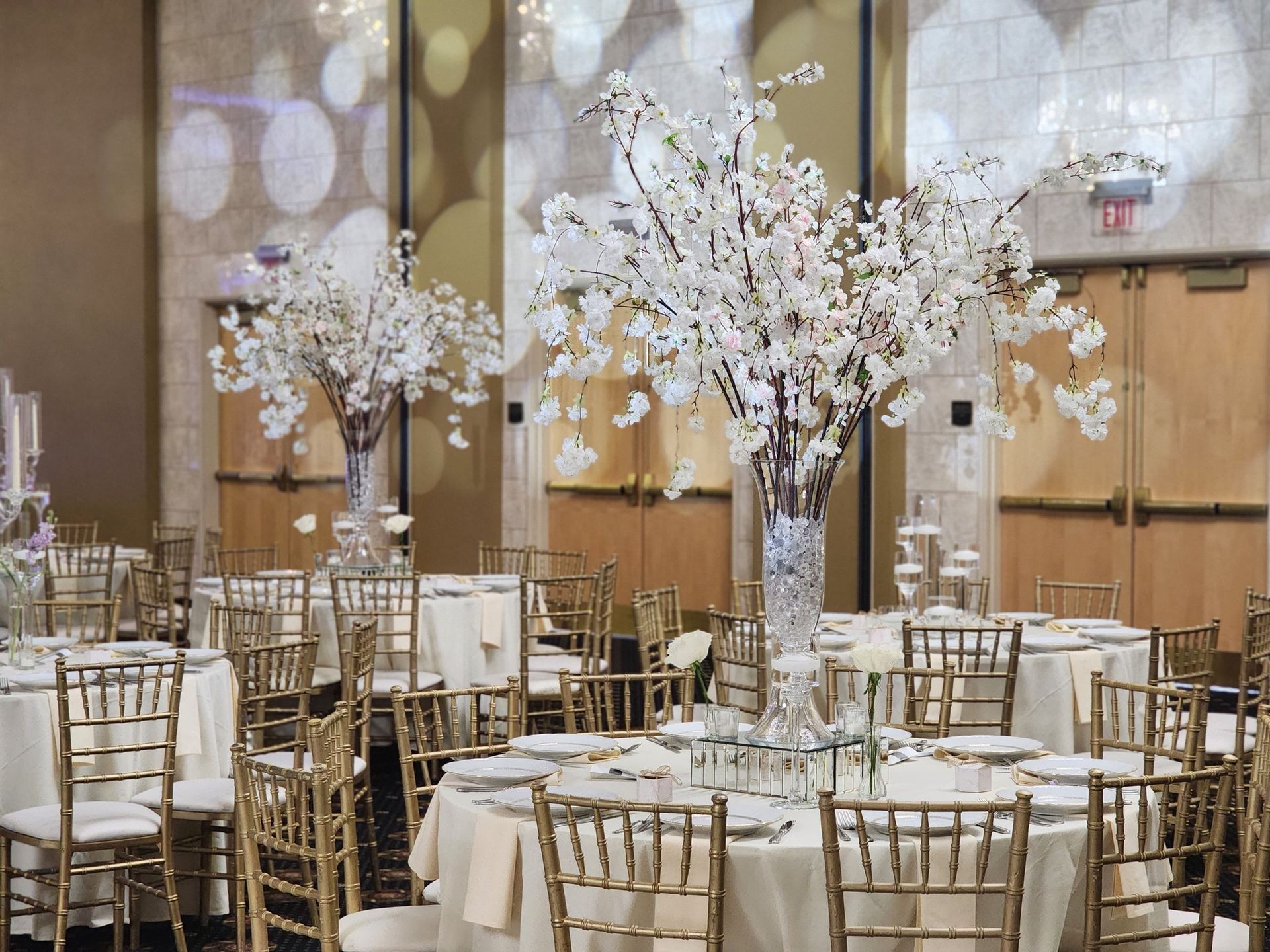 Banquet hall with round tables, gold chairs, and tall white floral centerpieces