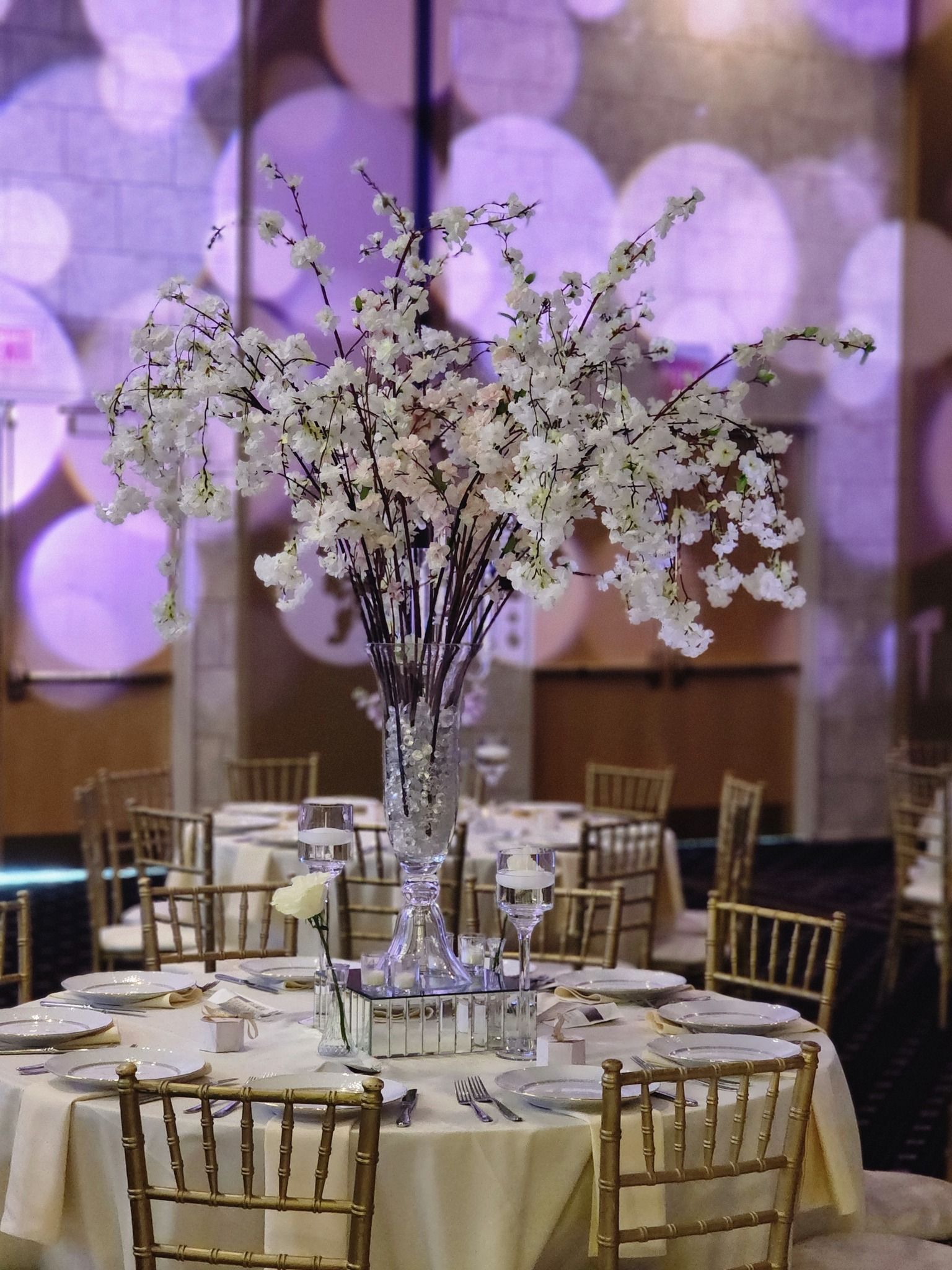 Round banquet table with white floral centerpiece and gold chairs in a softly lit event hall