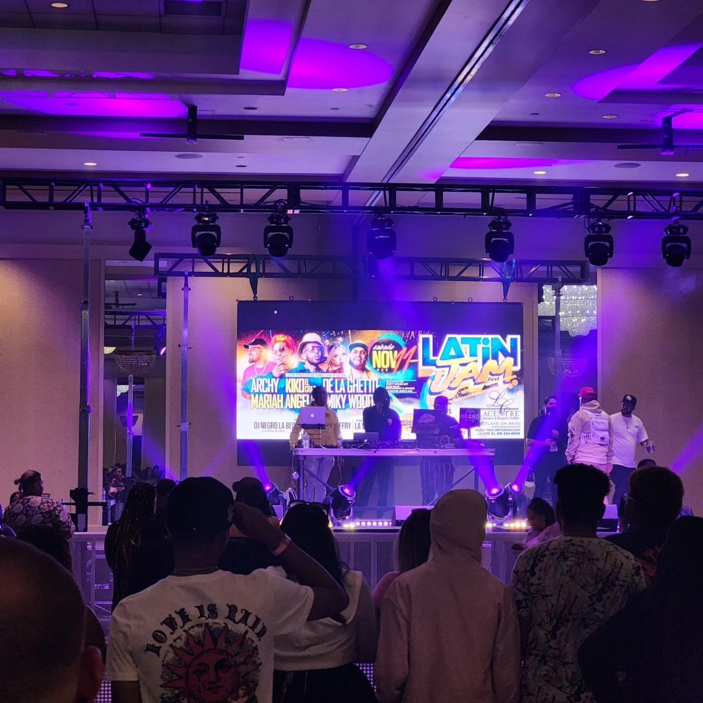 Live Latin music performance on a purple-lit stage with audience silhouettes in front