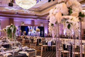 Elegant banquet hall with gold chairs, floral centerpieces, and a lit stage for a formal event