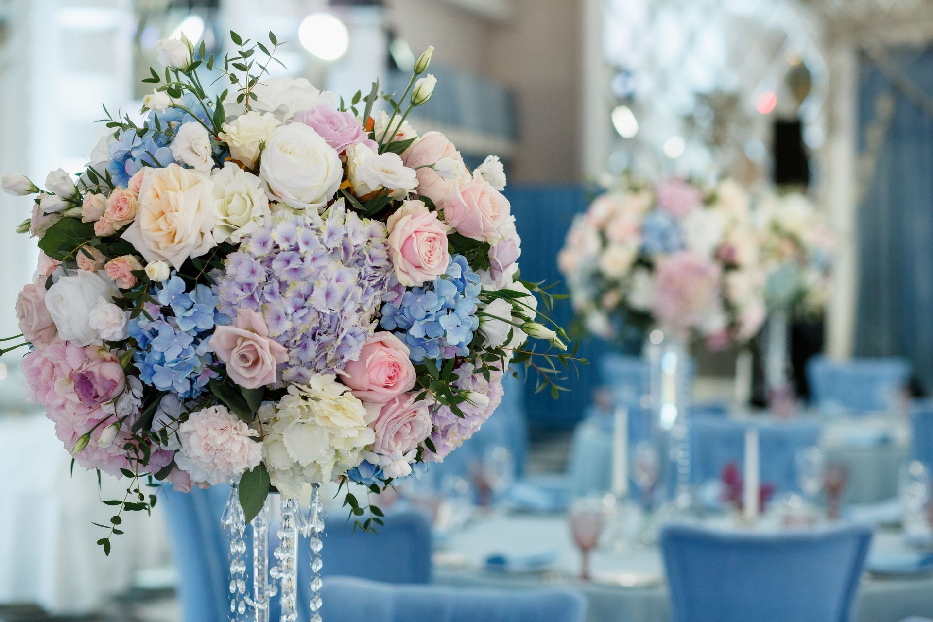 Pastel floral centerpieces on blue tables in a softly lit banquet hall
