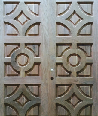 Ornate wooden double door with geometric carved panels and a central knob set.