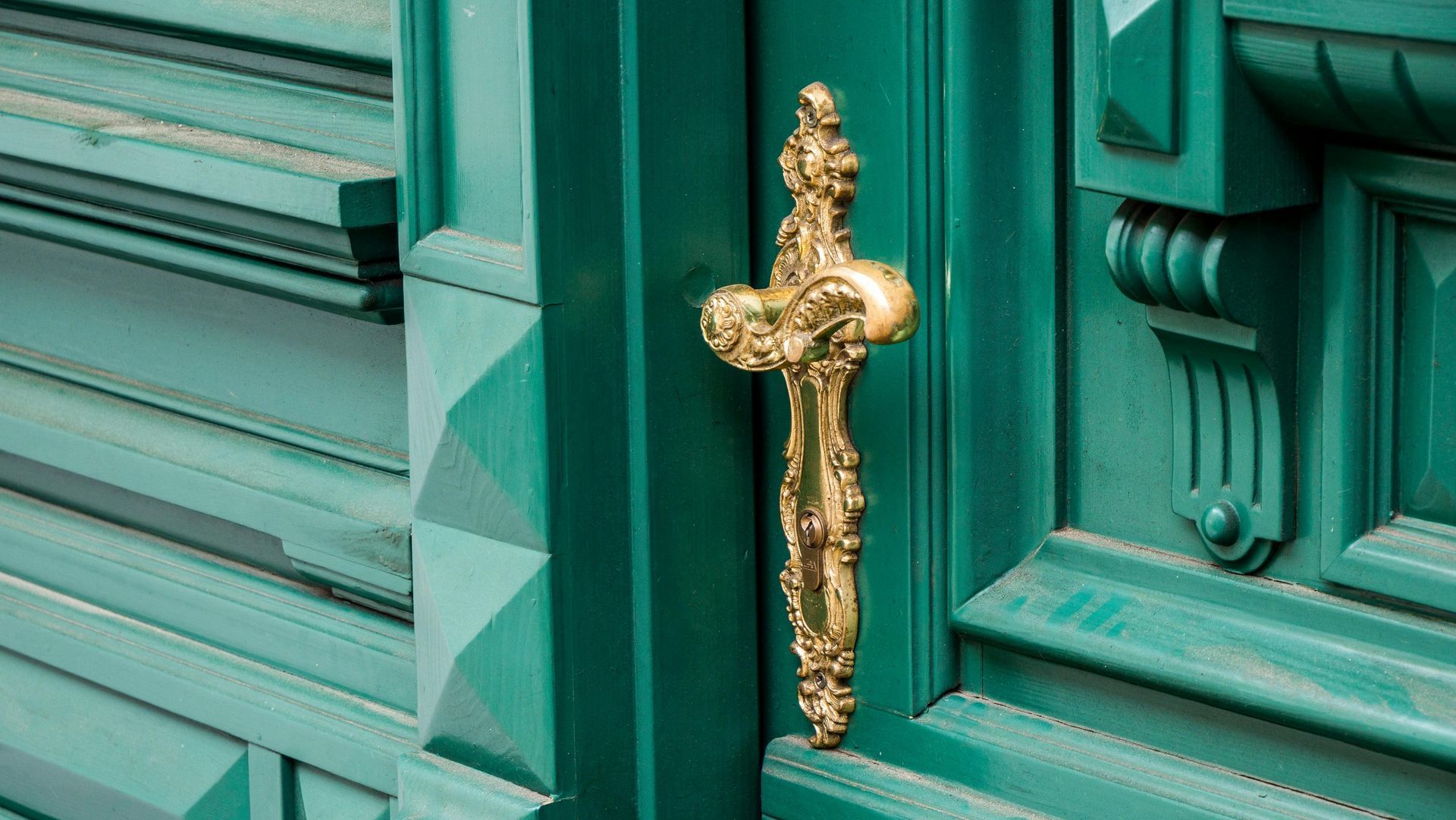 Gold ornate door handle on a teal painted door