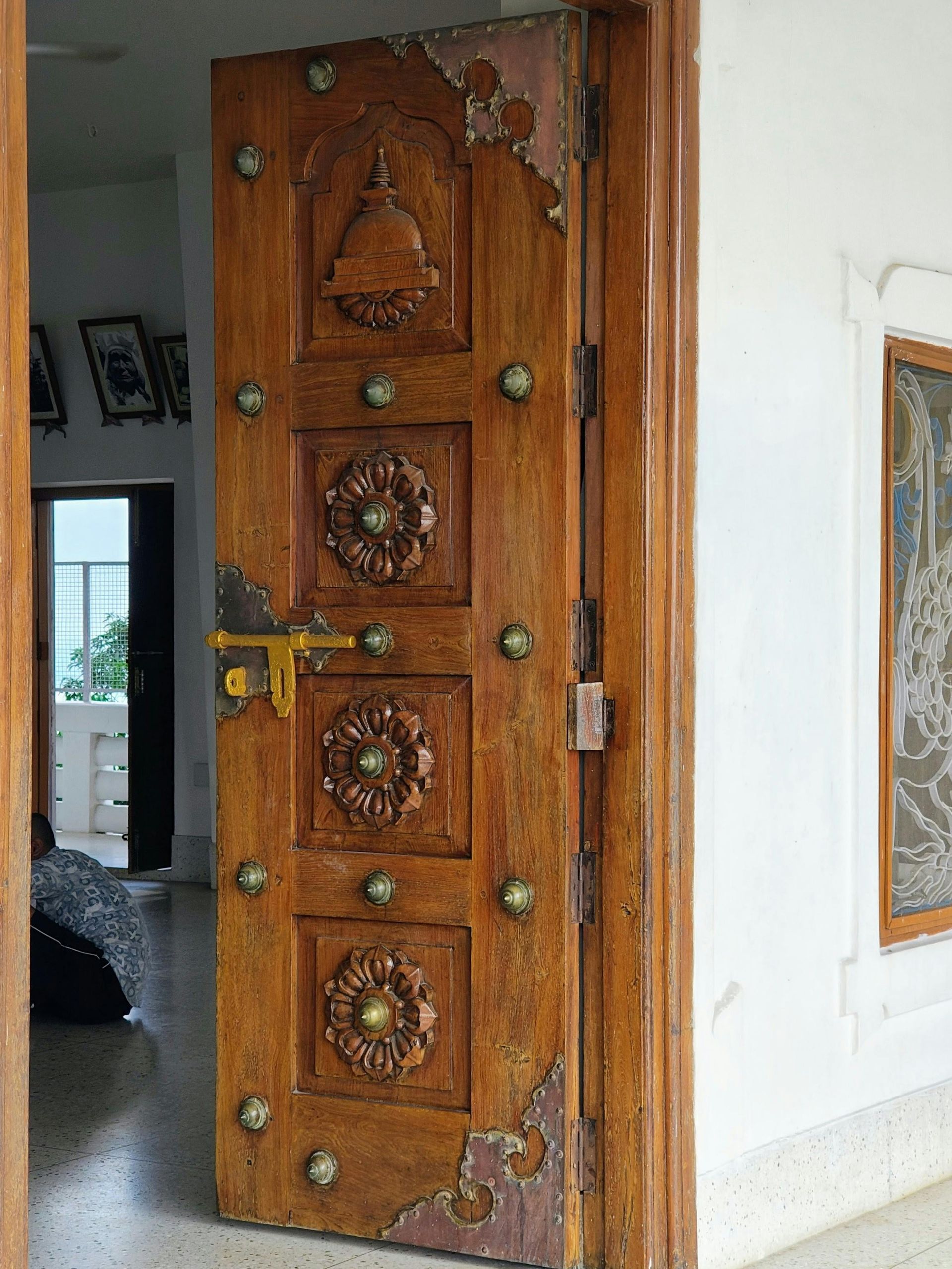 Carved wooden door with ornate brass details, slightly ajar in a white interior wall.