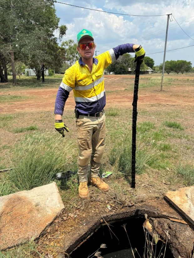 A Man in a Yellow and Blue Shirt is Standing Next to a Manhole Cover — Ecotreat Solutions NT in Winnellie, NT