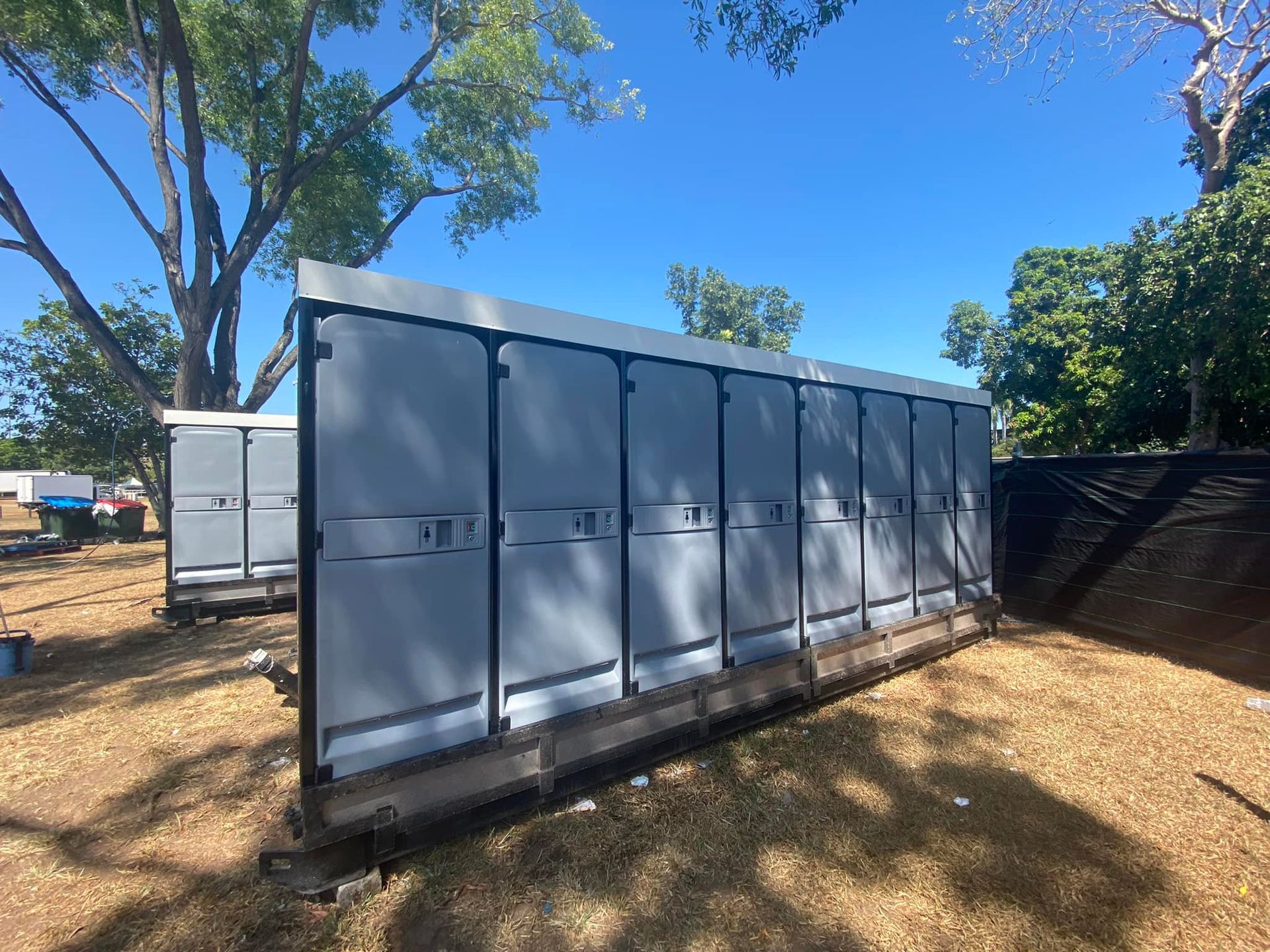 Portable toilets are lined in a row on the grass on a sunny day — Ecotreat Solutions NT in Winnellie, NT
