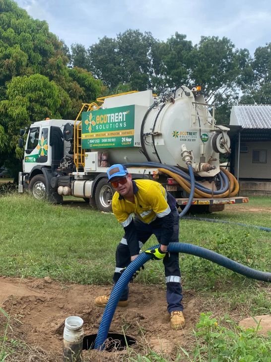 A Man is Standing in Front of a Vacuum Truck Holding a Hose — Ecotreat Solutions NT in Winnellie, NT
