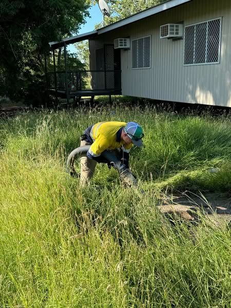 A Man is Kneeling in the Grass in Front of a House — Ecotreat Solutions NT in Humpty Doo, NT