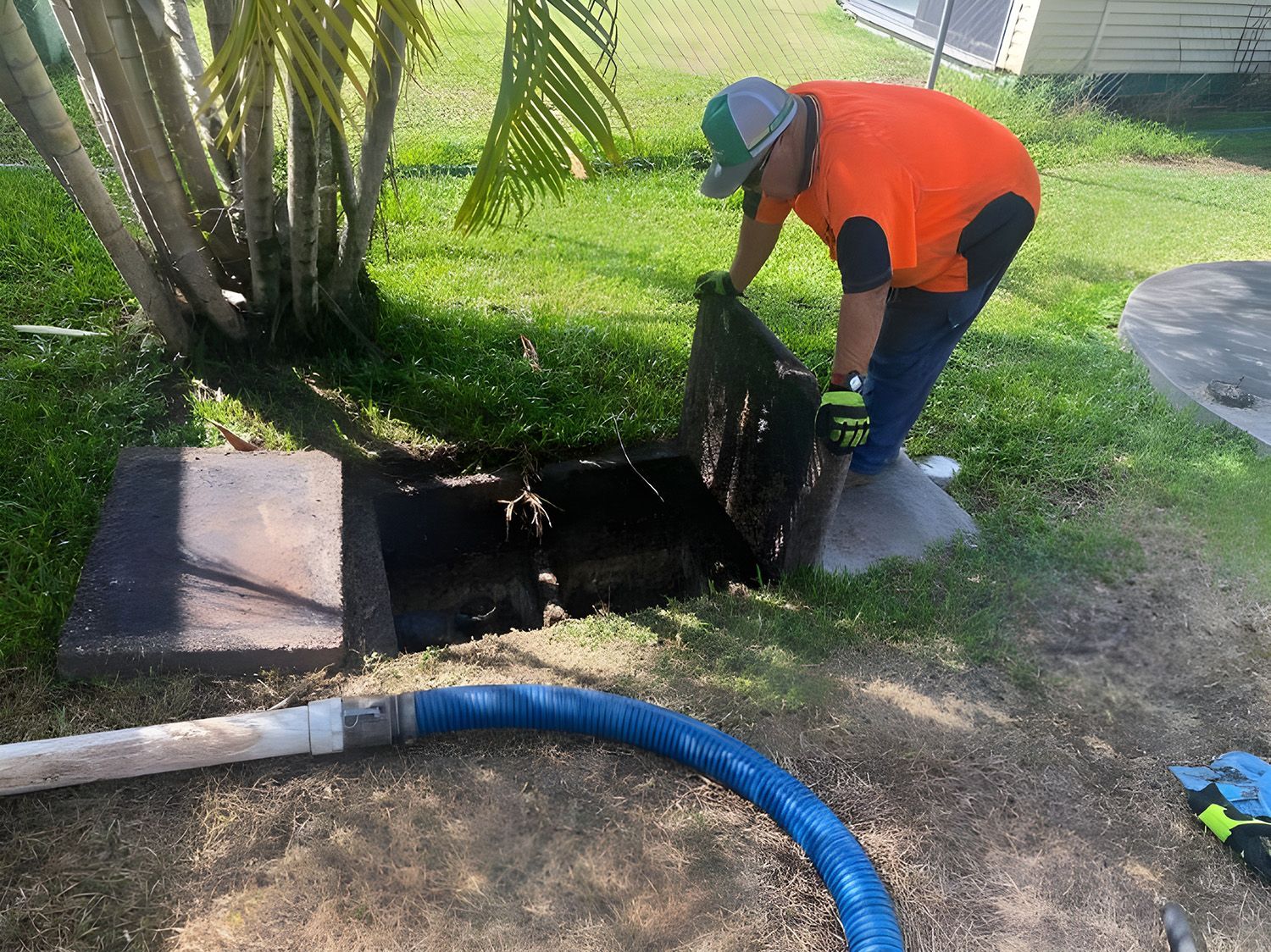 Man In Orange Shirt Opening A Septic Tank Cover