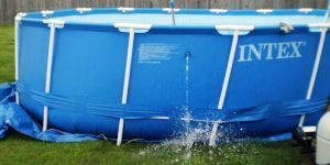 Blue Intex above-ground pool with water spraying from a leak near the base