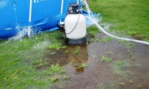 Propane tank with hoses on wet grass beside a blue pool, with water pooling nearby