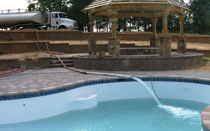 Backyard pool with blue water, stone patio, and a gazebo under construction in the background