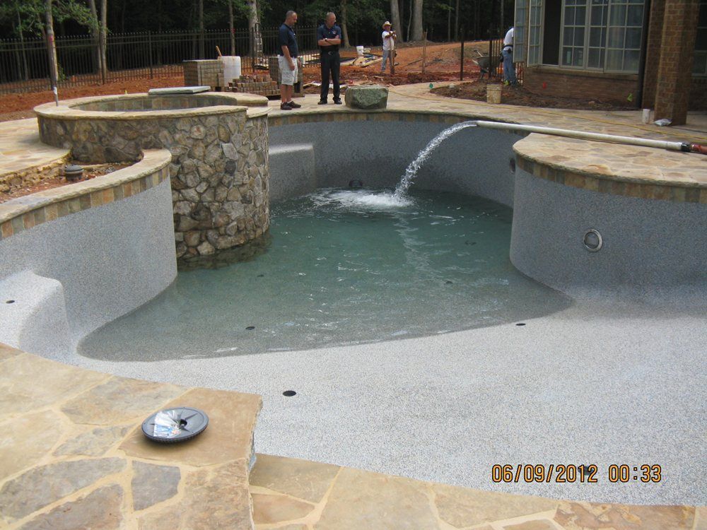 Empty stone pool with a fountain and a few people standing on the deck in the background