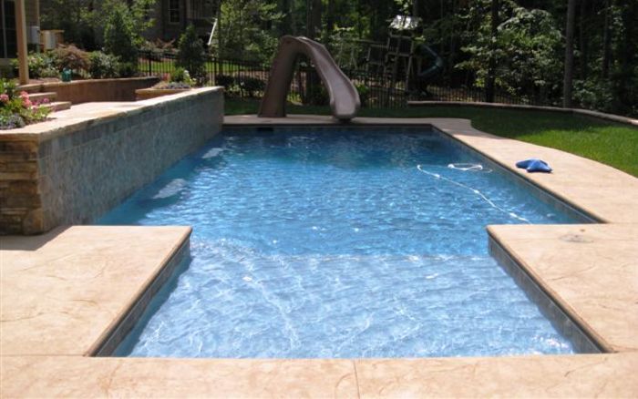 Backyard swimming pool with blue water, stone deck, and a small slide at the far end