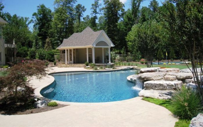 Backyard pool with curved stone edges, a small gazebo, and trees in the background