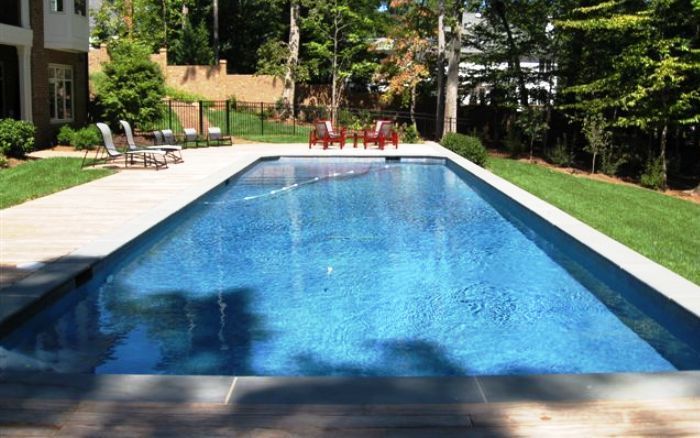 Backyard swimming pool with blue water, white deck, and lounge chairs in a sunny garden