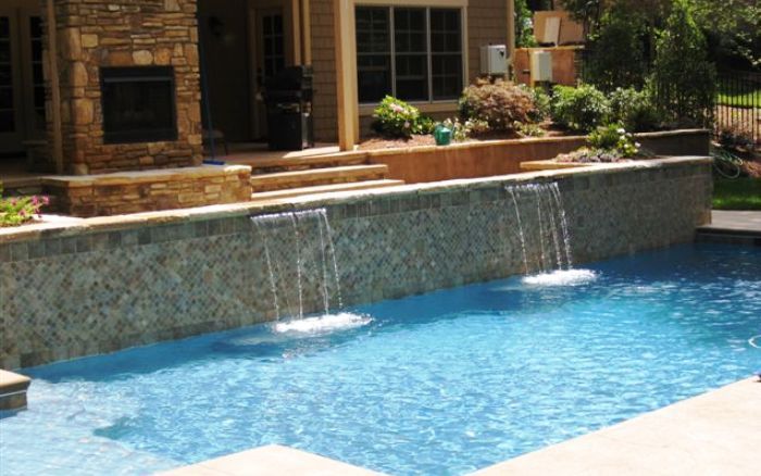 Backyard swimming pool with a stone waterfall and patio beside a house