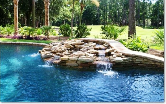 Backyard pool with blue water and a stone waterfall surrounded by lush greenery