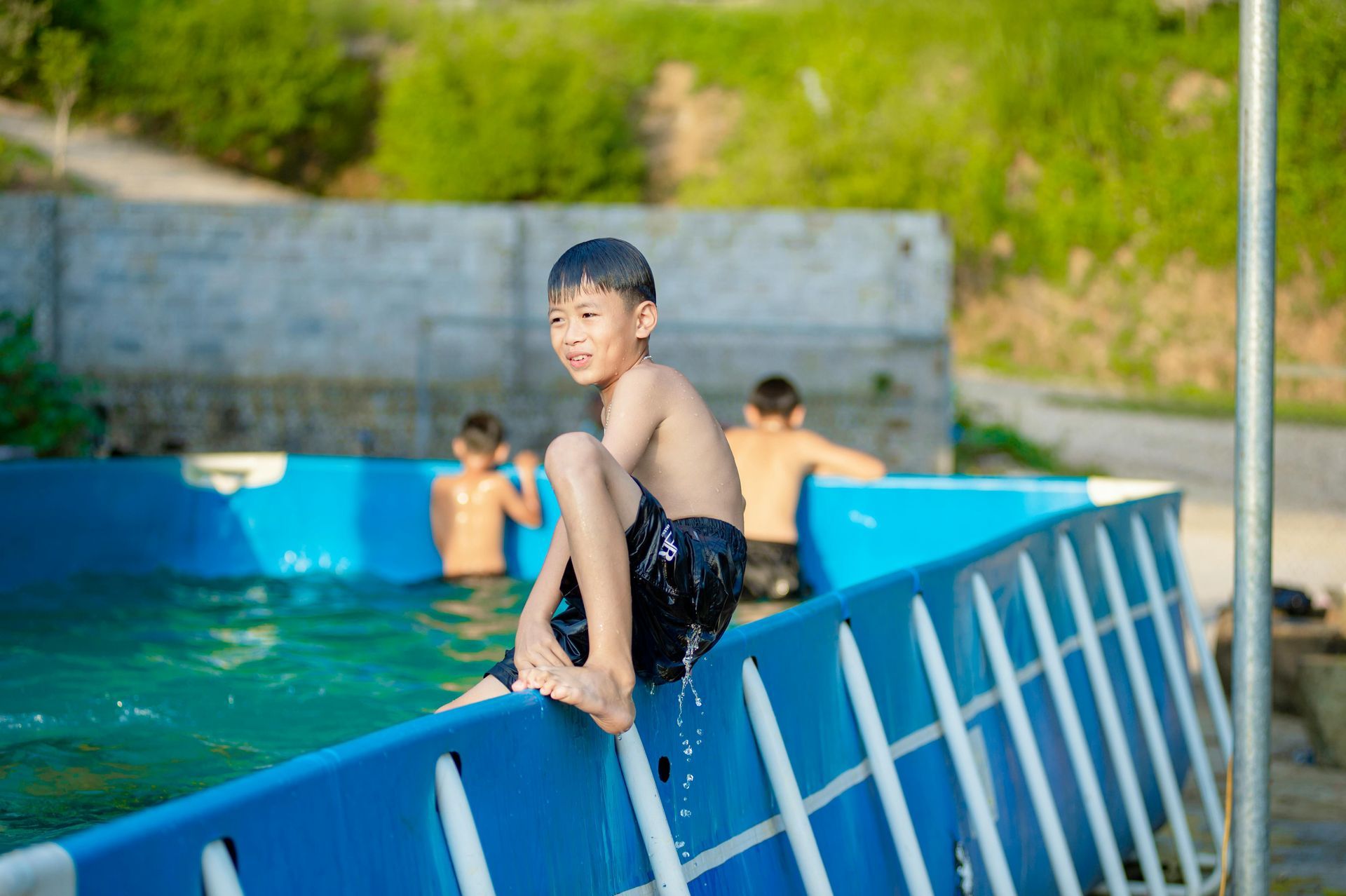 Boy sitting on a blue pool barrier with swimmers in the background