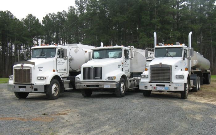 Three white cement mixer trucks parked side by side on gravel in a wooded lot