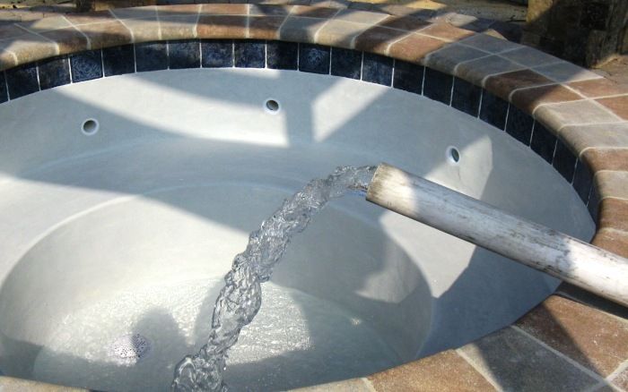 Water filling an empty hot tub with a hose over the tiled edge