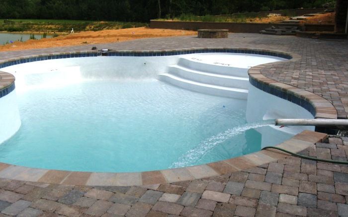 Backyard swimming pool with light blue water, stone decking, and built-in steps